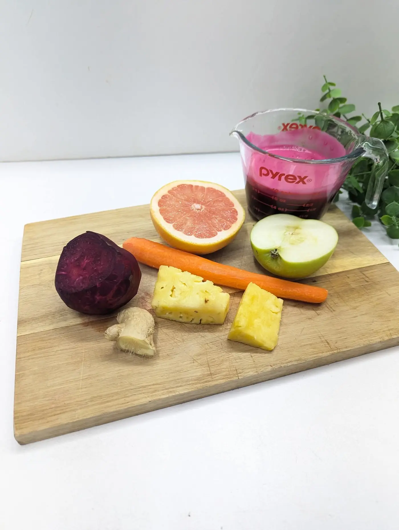 Ingredients for Beet Booster juice — beet, grapefruit, carrot, apple, pineapple and ginger — beside a cup of fresh beet juice