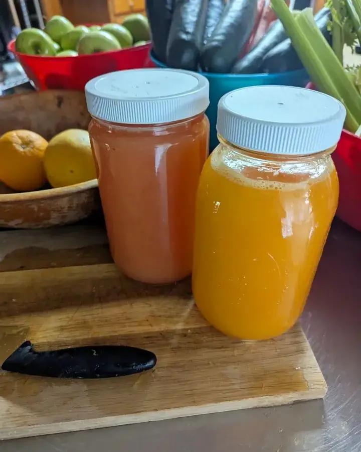 Two jars of fresh-pressed juice on a cutting board with apples, oranges and celery