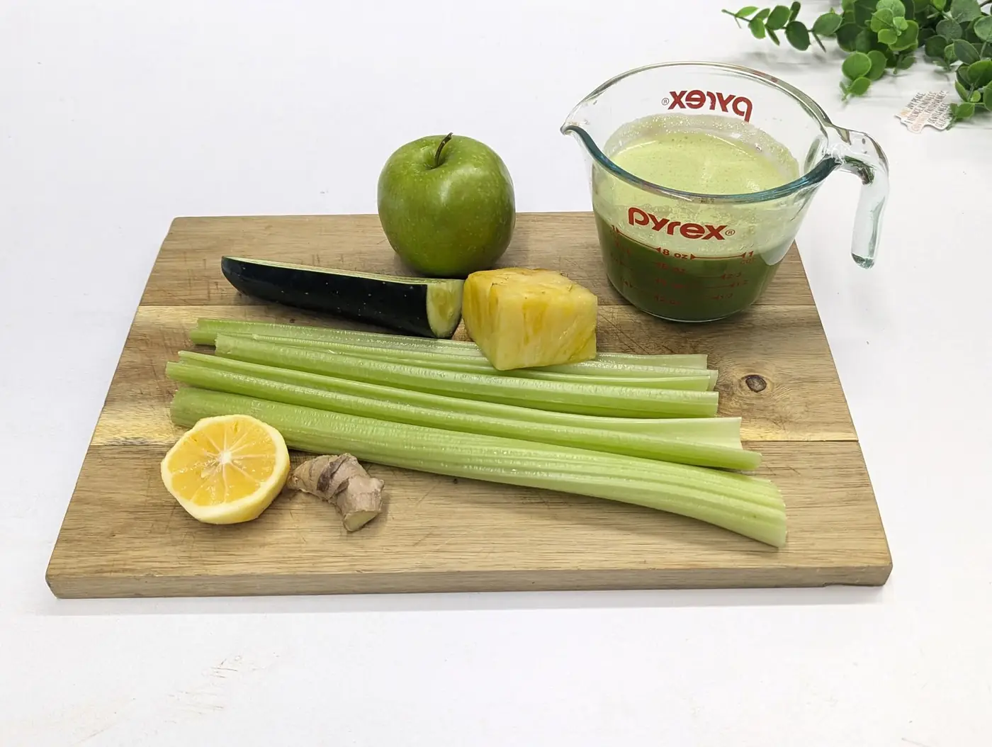 Ingredients for a green juice — apple, cucumber, celery, lemon, ginger and pineapple — beside a cup of fresh green juice