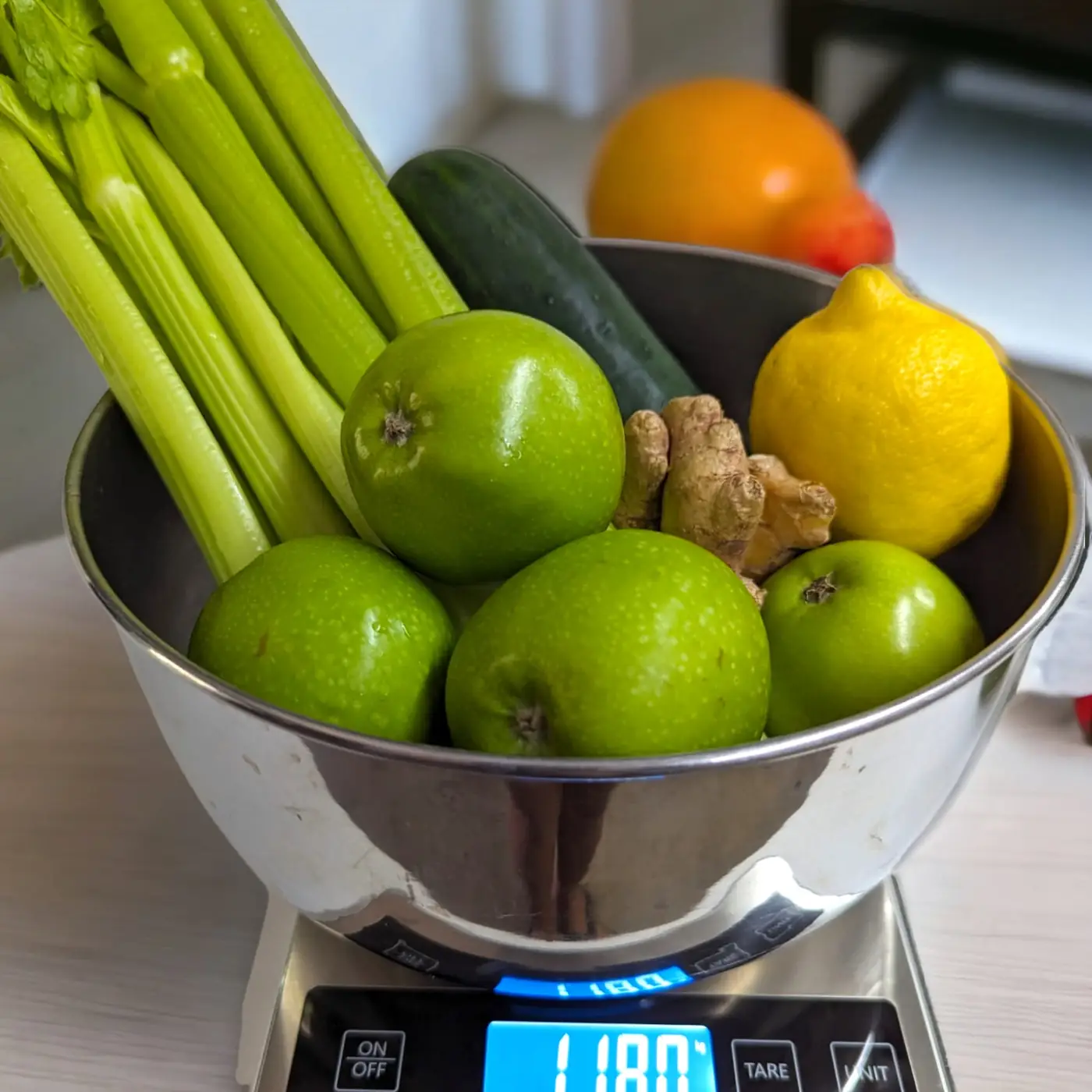 A bowl of celery, green apples, cucumber, ginger and lemon on a kitchen scale