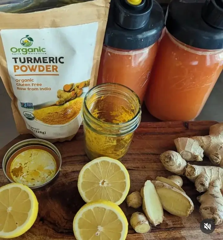 Organic turmeric with fresh ginger and lemon beside bottles of golden wellness juice